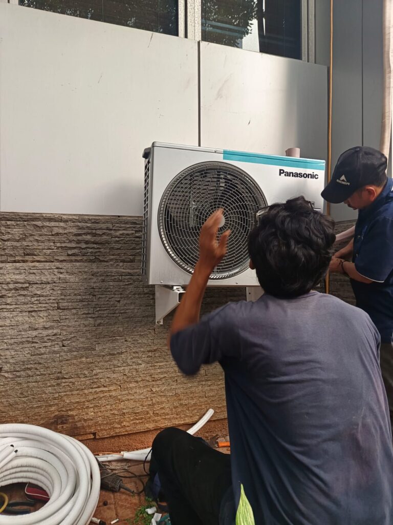 Teknisi sedang melakukan perbaikan outdoor AC tampak selang AC disampingnya